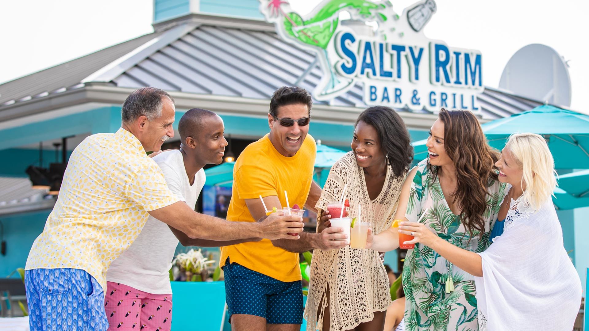 Group of people toast with drink cups outside the Salty Rim Bar and Grill at Margaritaville Resort Orlando.