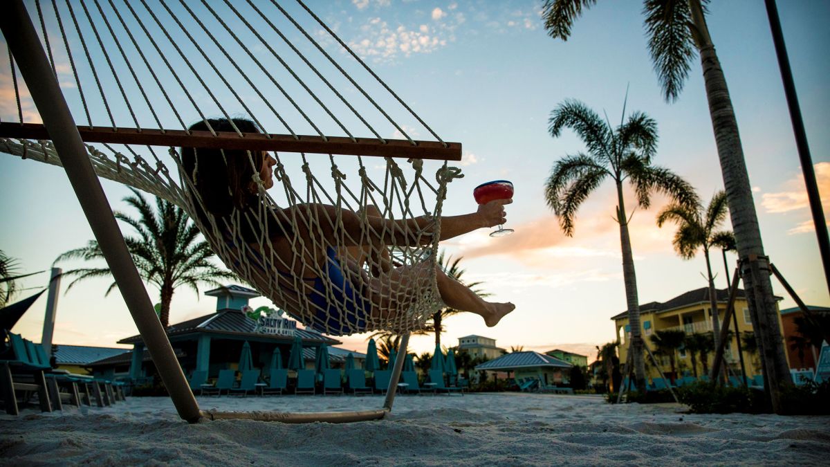Woman relaxing with a drink on a hammock on the sand at Fins Up Beach Club.