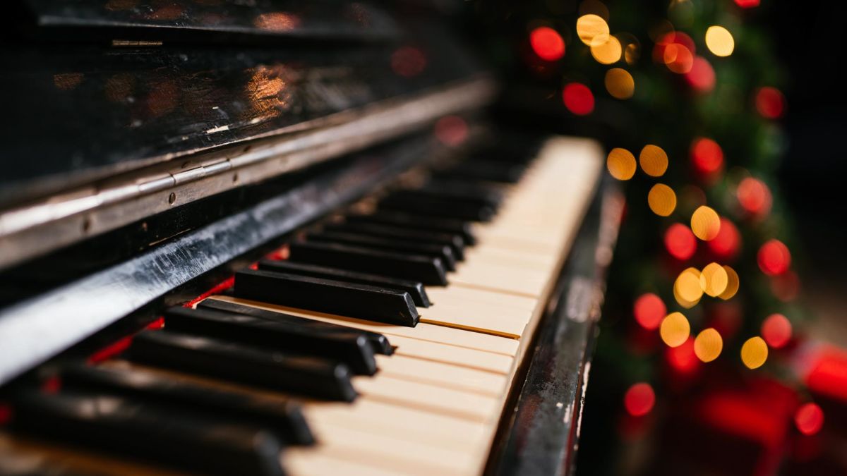Close-up of a piano in front of a lit Christmas tree.