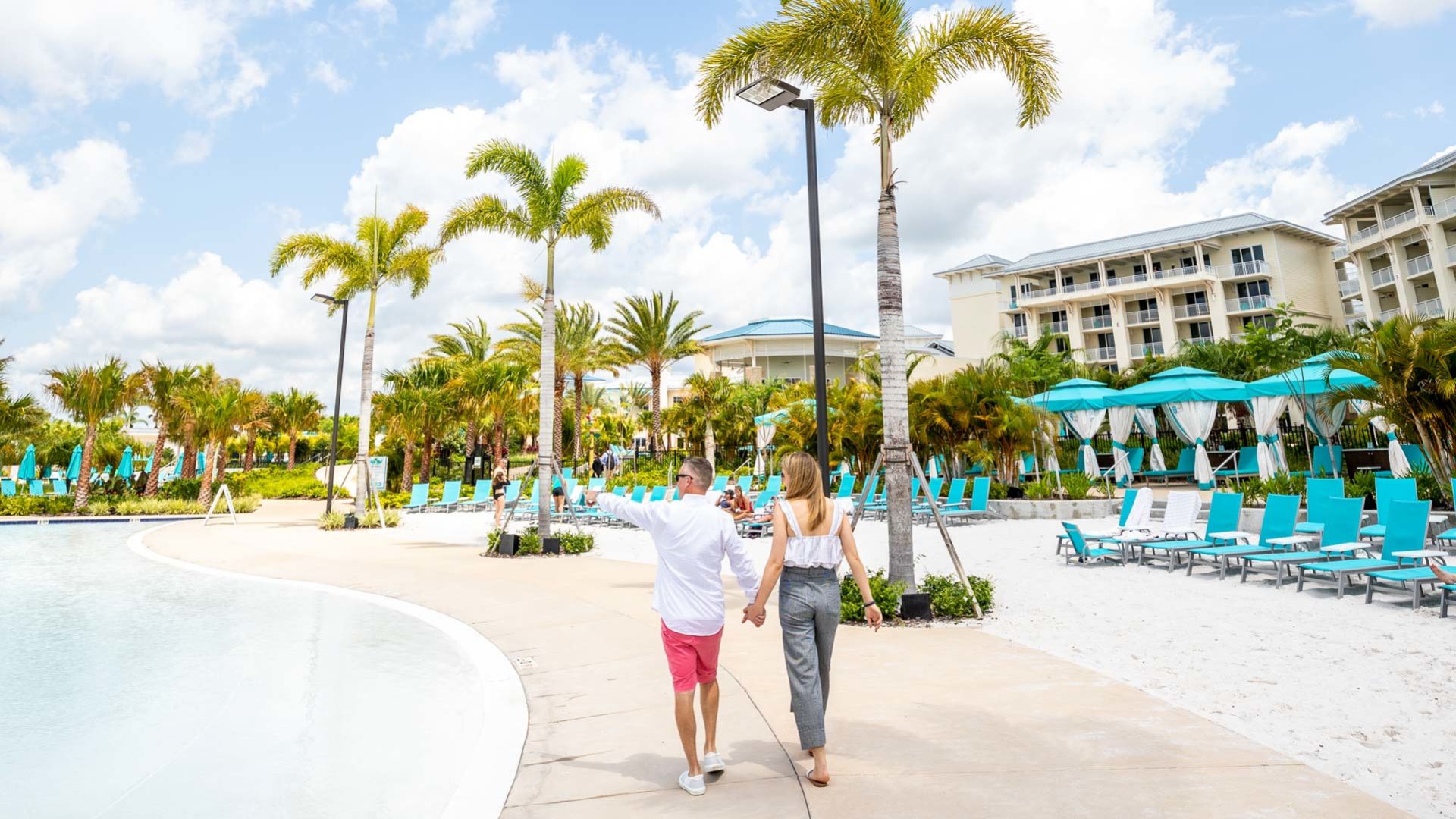 Couple holding hands while walking through the Fins Up Beach Club and pool.