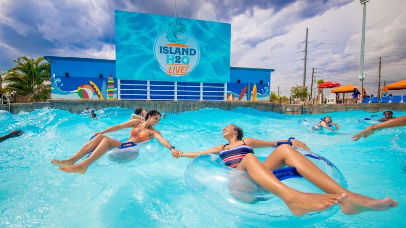 Two friends holding hands while sitting in separate tubes in the Island H2O Live! water park wave pool.