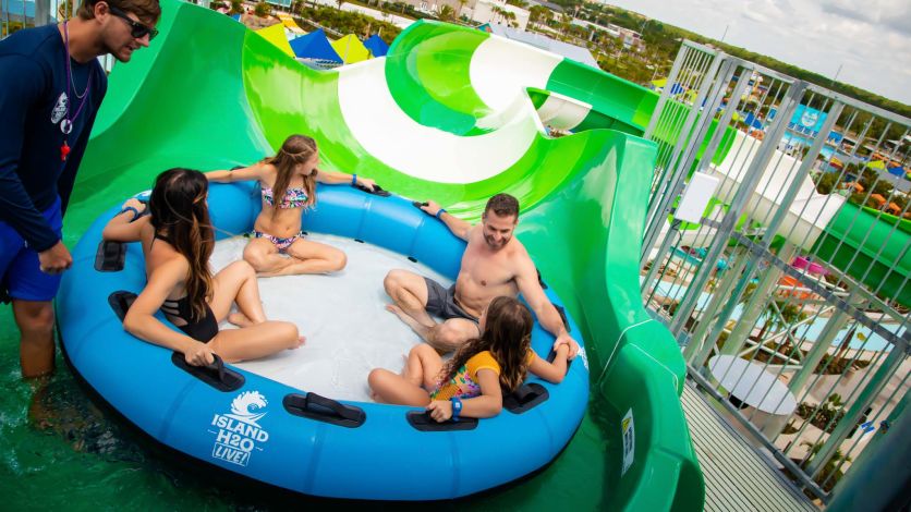 Family of a mother, father, and two daughters sit in a large ride tube preparing to slide down the Hashtag Heights water slide at Island H2O Live! Water Park.