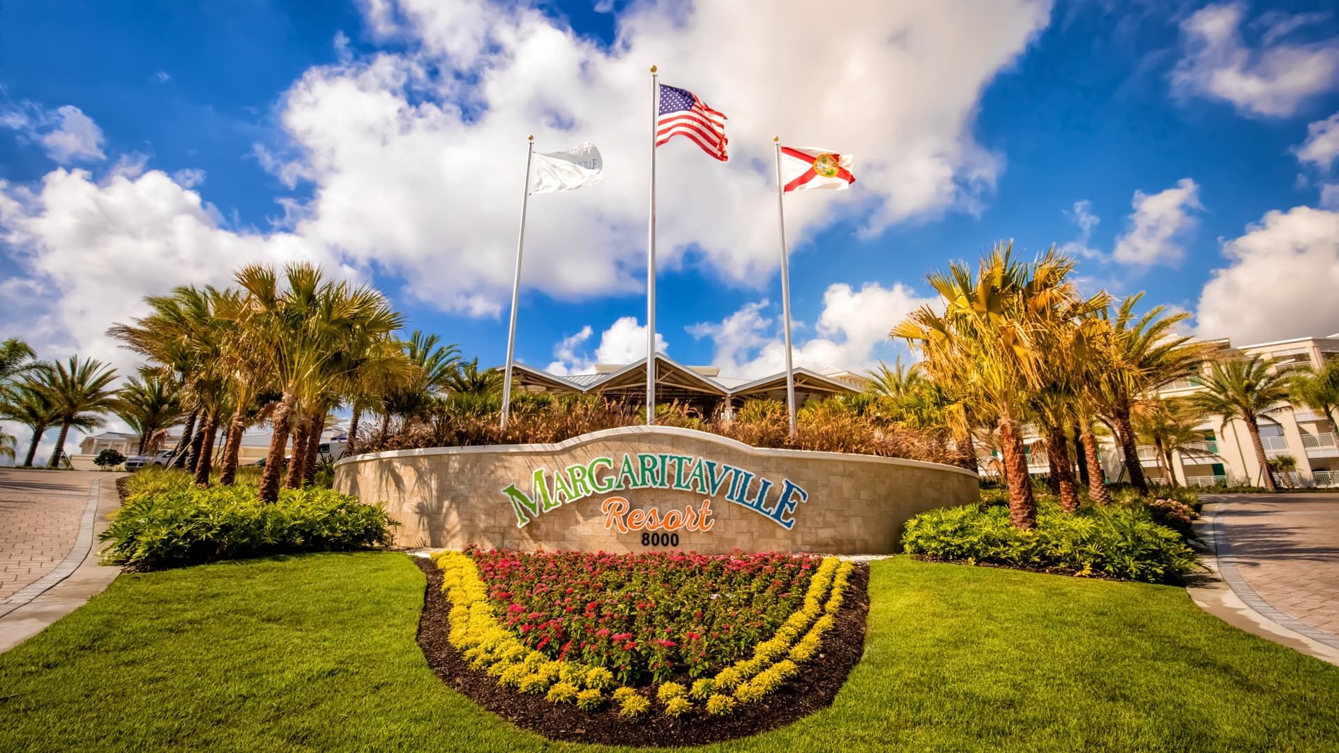 Flags of the United States, Florida, and Margaritaville fly above a garden at the entrance of Margaritaville Resort Orlando.