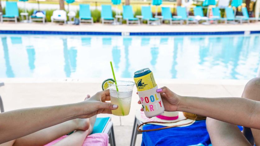 Friends toasting a margarita and a beer can next to the pool at Margaritaville Resort Orlando