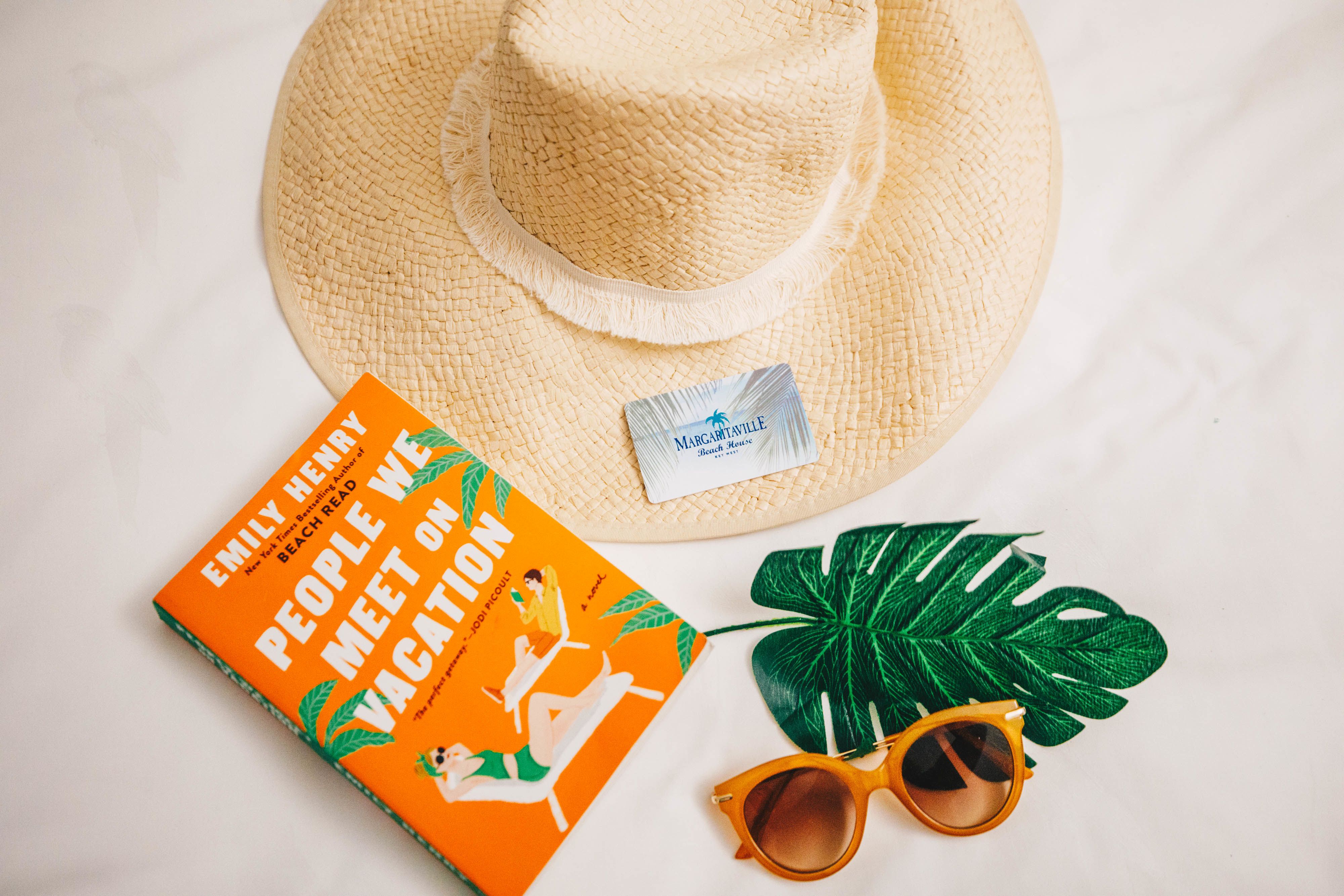 Straw hat with a book and sunglasses and hotel room key