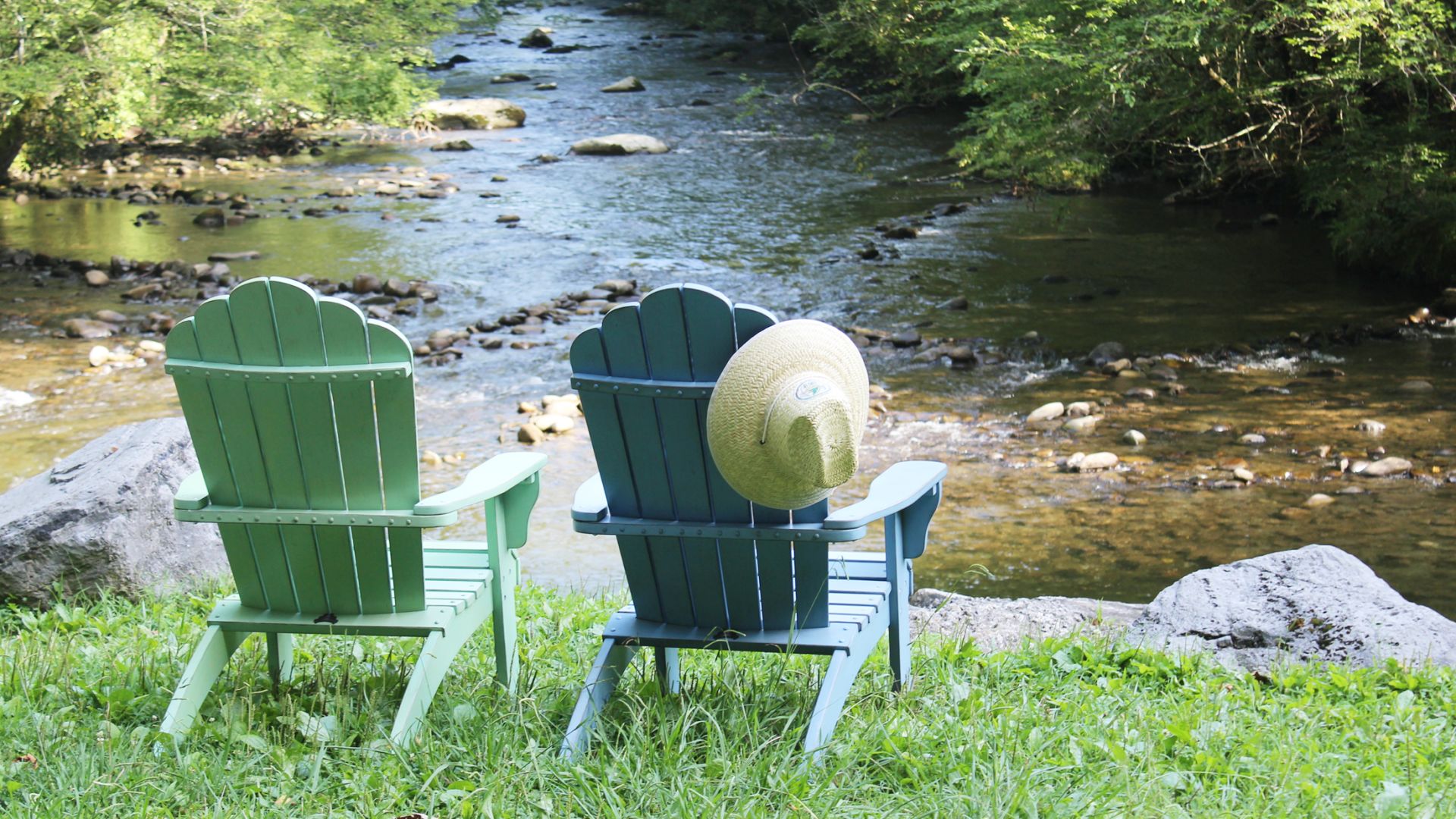 A Couple Of Chairs Next To A River With A Large Rock In The Middle