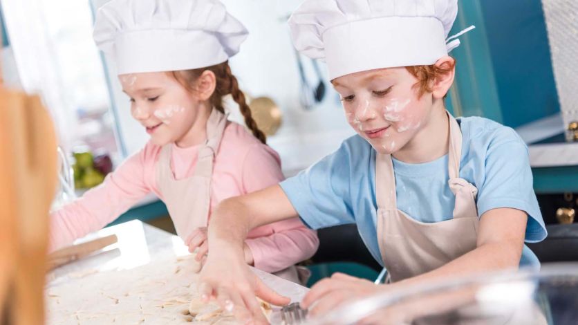 Young kids wearing chef hats and aprons while making cookies