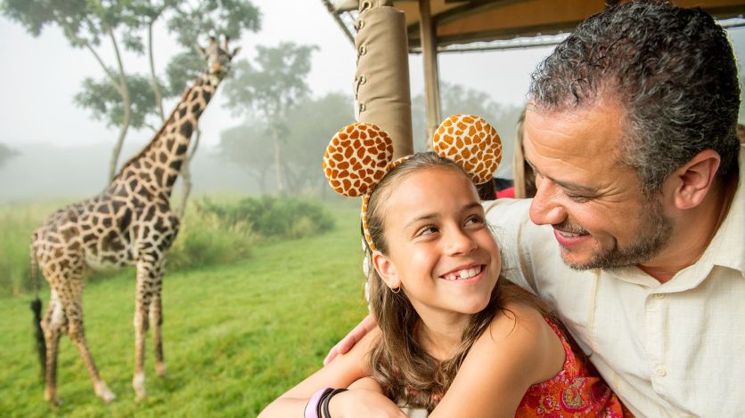 A father and daughter on the Kilimanjaro Safaris ride at Disney’s Animal Kingdom looking at a giraffe.