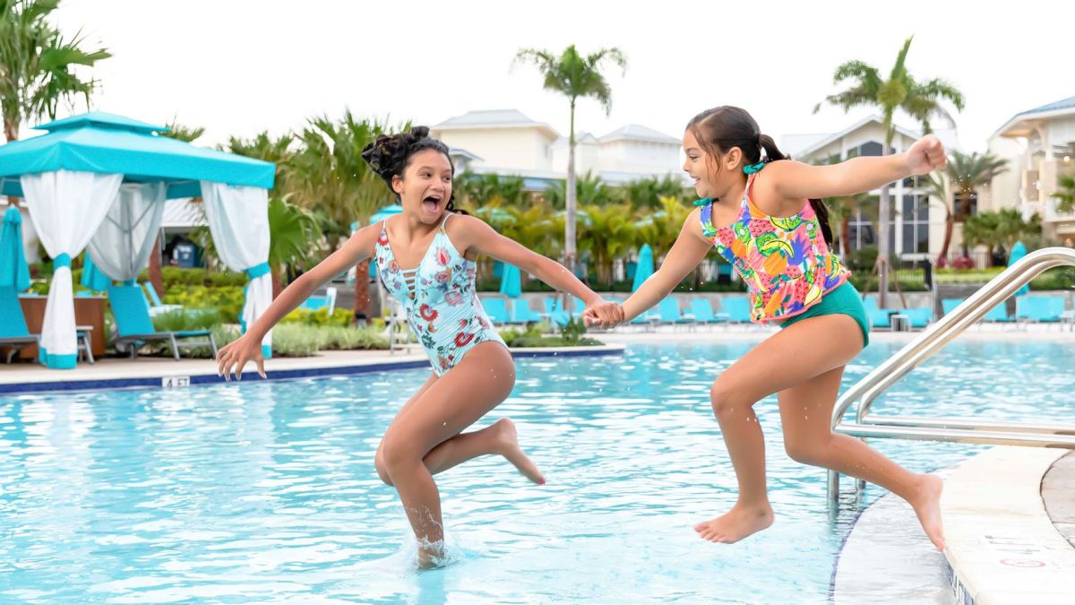 Two young girls holding hands as they jump into the Fins Up Pool.